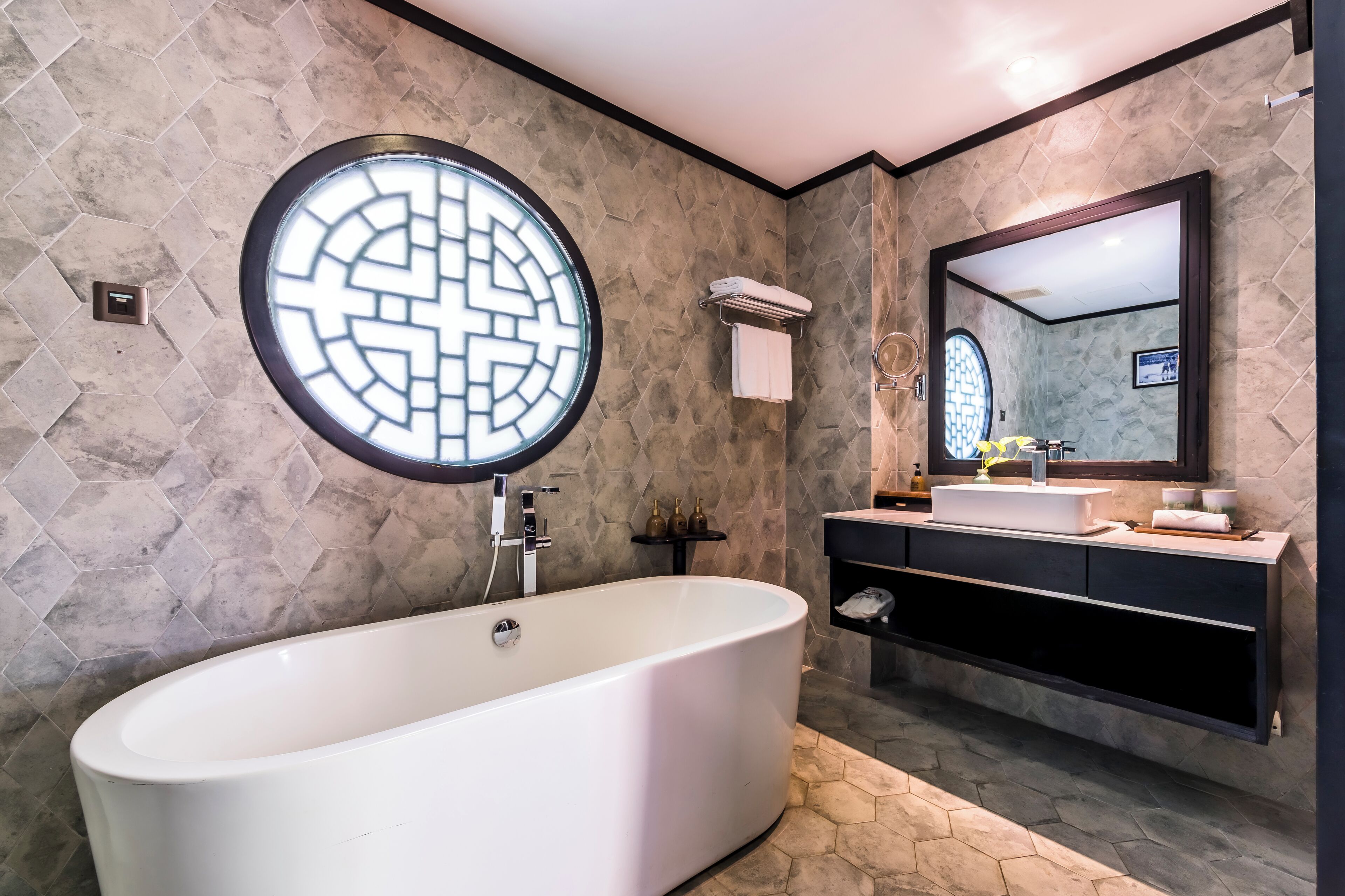A modern bathroom with a freestanding bathtub, a round mirror with a geometric design, and a vanity with a sink and storage.