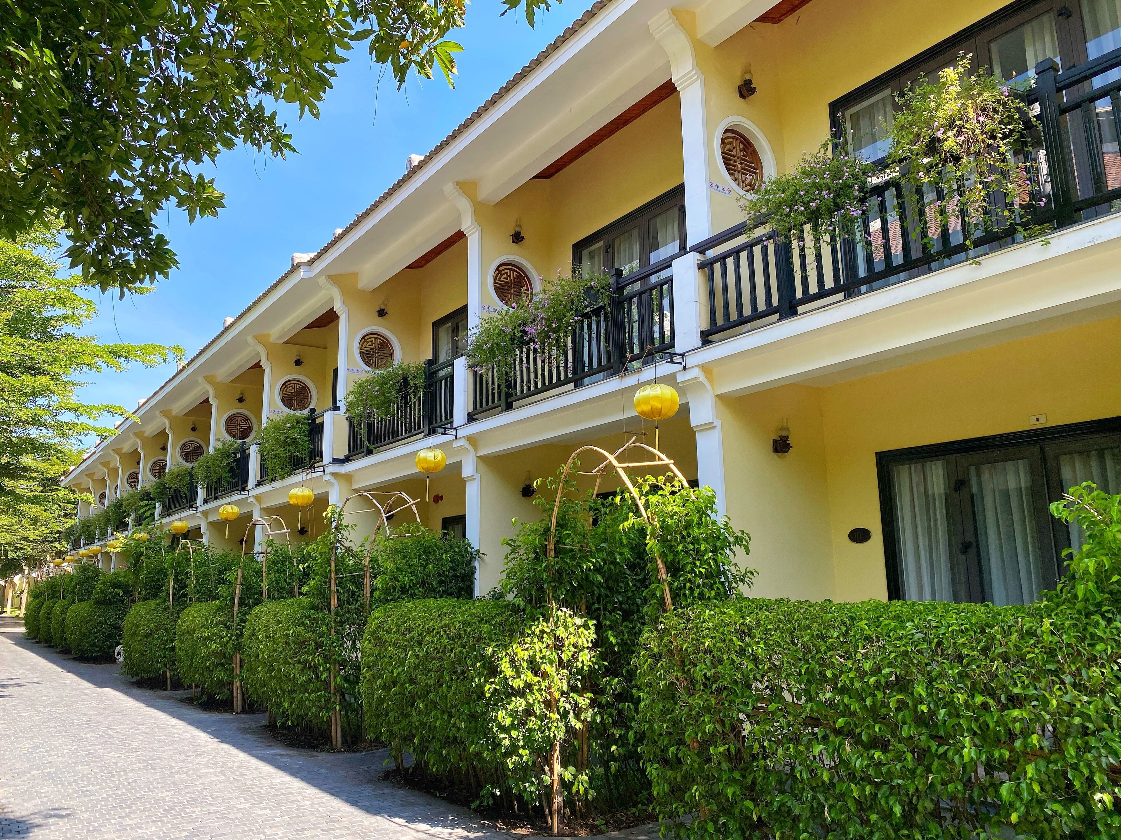 A row of hotel balconies with plants and yellow lanterns.