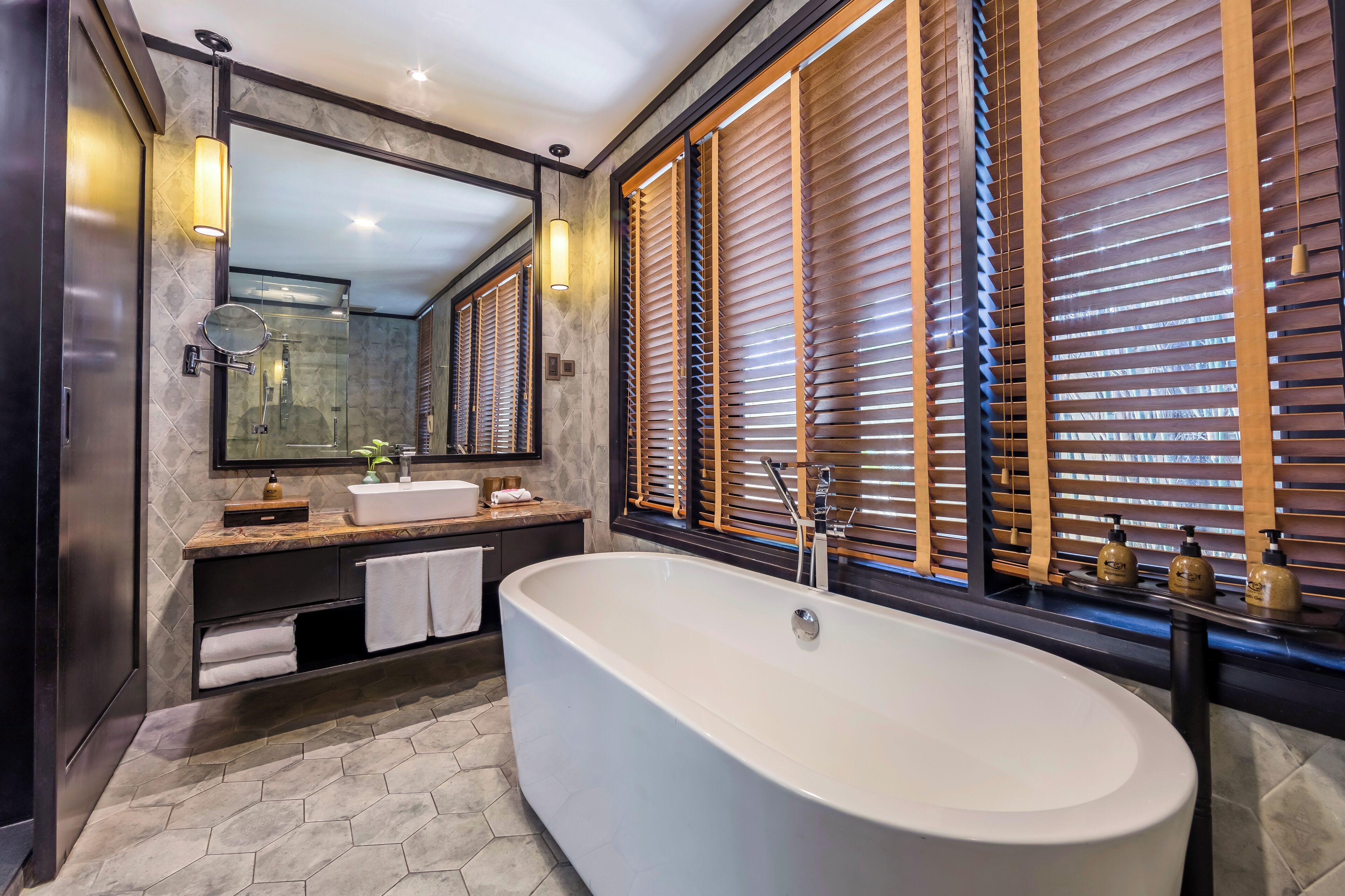 A modern bathroom with a freestanding bathtub, a large mirror, and wooden blinds.