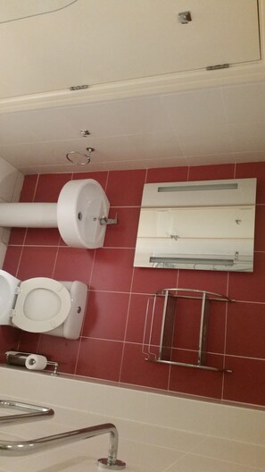 A bathroom with a toilet, sink, and handrail.