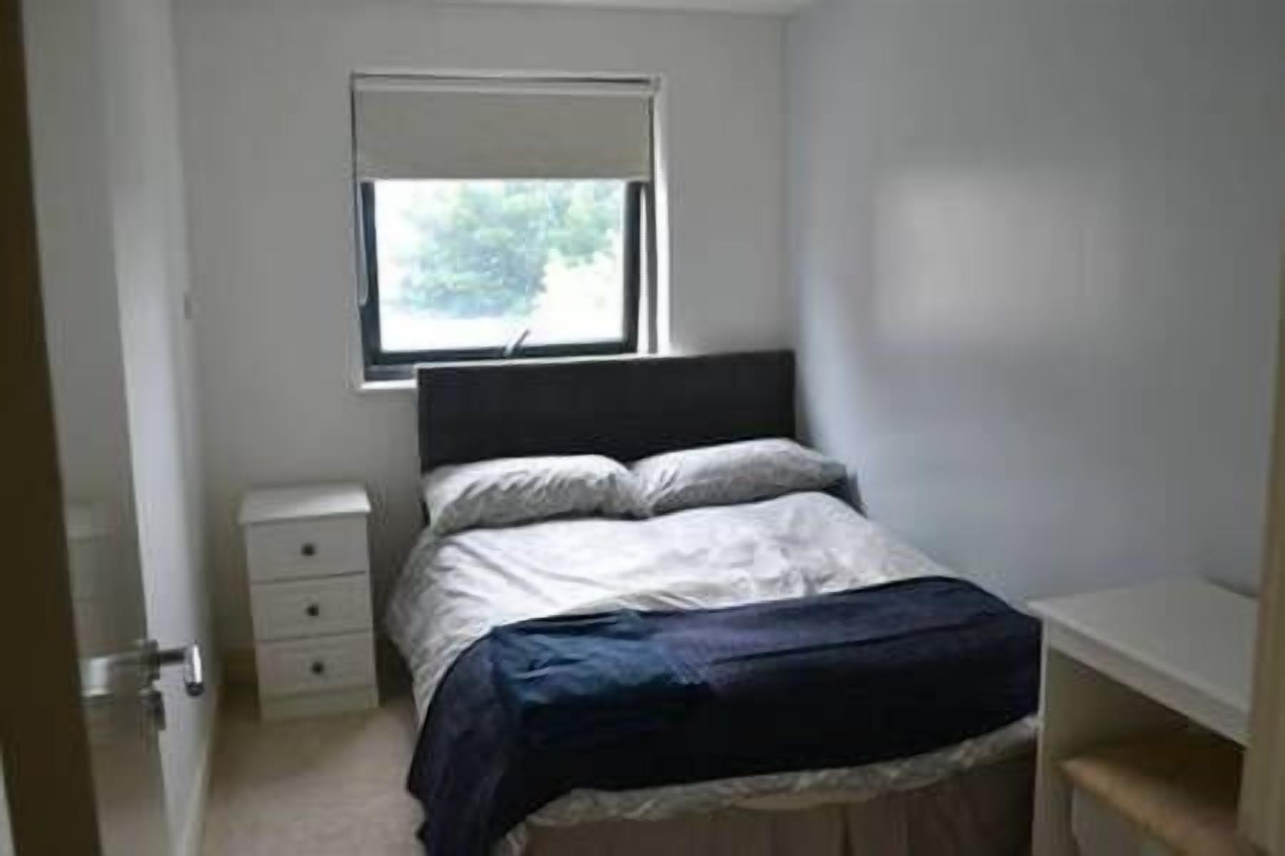 A bedroom with a bed, a nightstand, a window, and a bench.