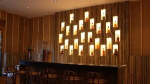 Una zona de bar con una pared de madera y varias botellas iluminadas. Hay varias sillas de madera dispuestas alrededor de la barra.
