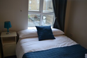 A bedroom with a bed, a nightstand with a lamp, and a window with curtains. - Jervis Place Apartment (Dublin)