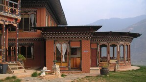 A traditional building with a reception area, stone steps, and a mountainous backdrop. - Dewachen Resort (Paro)