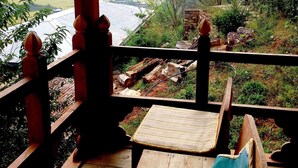 A wooden deck with a single chair and a small table, overlooking a natural landscape with trees and a body of water. - Dewachen Resort (Paro)