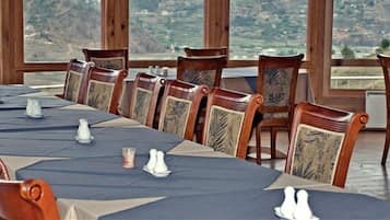 A long dining table set with chairs, salt and pepper shakers, and a candle, with a scenic view through large windows.