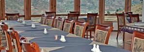 A long dining table set with chairs, salt and pepper shakers, and a candle, with a scenic view through large windows. - Dewachen Resort (Paro)