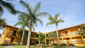 A hotel with multiple yellow buildings, palm trees, and a clear sky. - Águas de Palmas Resort (Governador Celso Ramos)