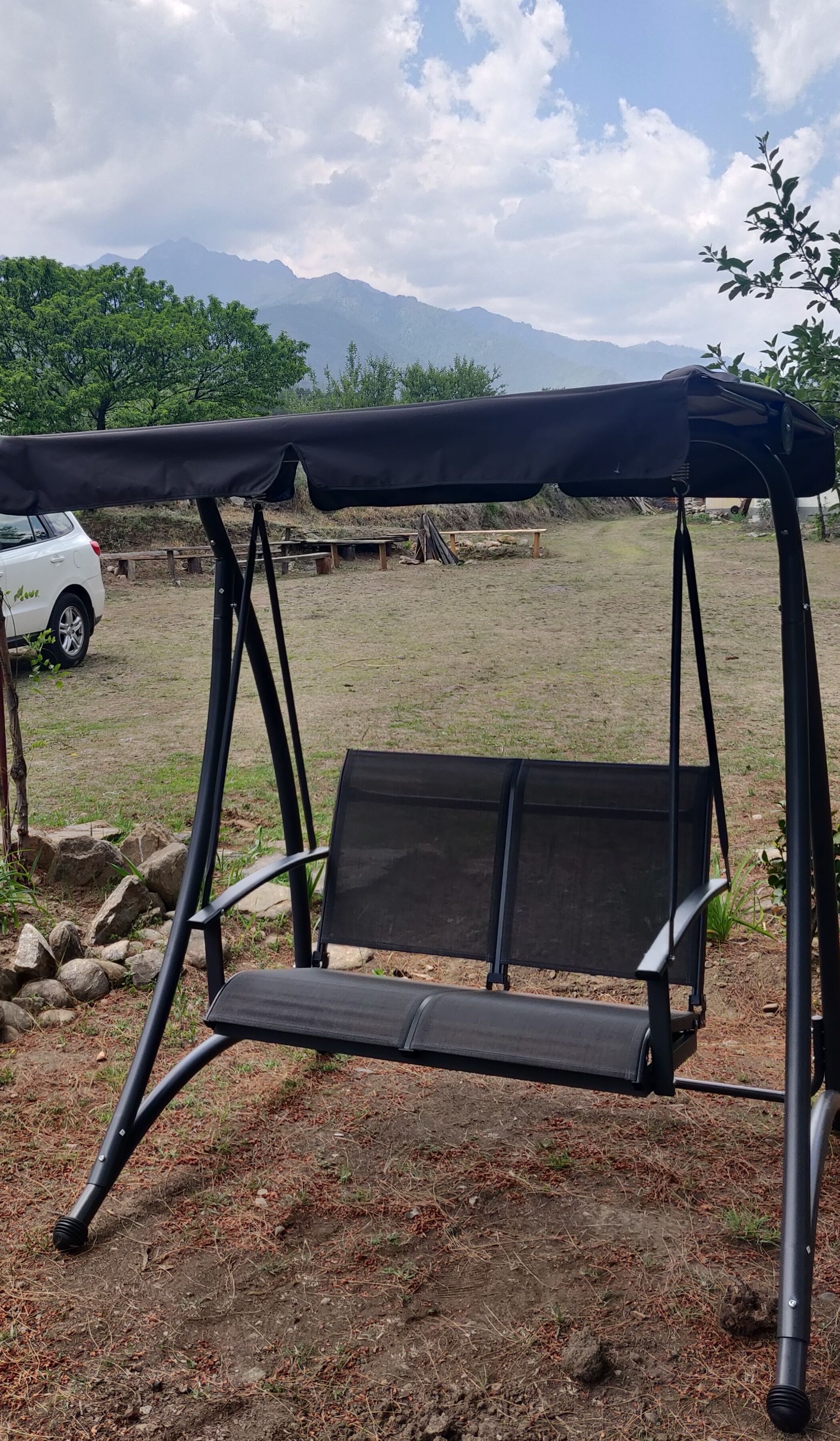 A black camping chair with a canopy, set on a grassy field with mountains in the background.