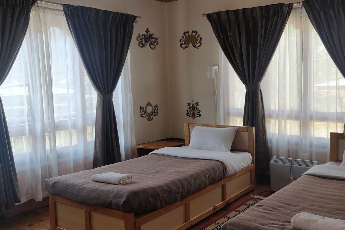 Une chambre d’hôtel avec deux lits, une table de chevet, un radiateur et des rideaux.