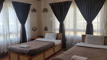 A hotel room with two beds, a bedside table, a heater, and curtains.