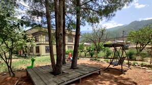 Une terrasse en bois rustique, agrémentée d’une balançoire, entourée de pins et avec une chaîne de montagnes en toile de fond.