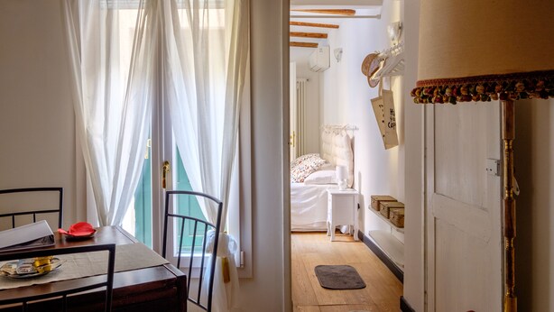 A room with a bed, a bedside table, a lamp, and a window with sheer curtains.