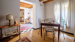 A dining area with a wooden table and chairs, a chandelier, and a view of a room with a checkered floor.