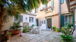 A courtyard with a stone floor, potted plants, a table with chairs, and a door with a lattice design.