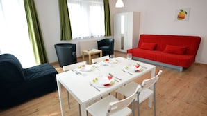 A modern living room with a dining table set for two, a red sofa, and a black bean bag. - Toldi Apartments (Pecs)