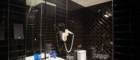 Un baño moderno con pared de azulejos negros, un lavamanos blanco, un inodoro y un cabezal de ducha de mano.