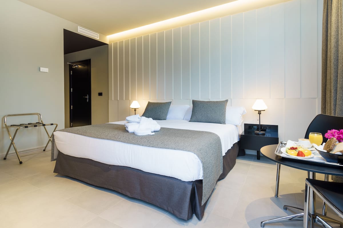 A modern hotel room with a large bed, bedside tables, a desk with breakfast, and a seating area.