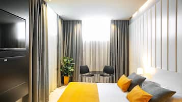 A hotel room with a bed, a TV, a dining table with chairs, and curtains.