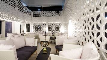A modern lounge area with white wicker furniture, a central coffee table, and a decorative hookah.