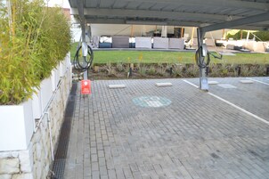 A parking area with a Tesla charging station, a covered seating area, and a grassy patch.