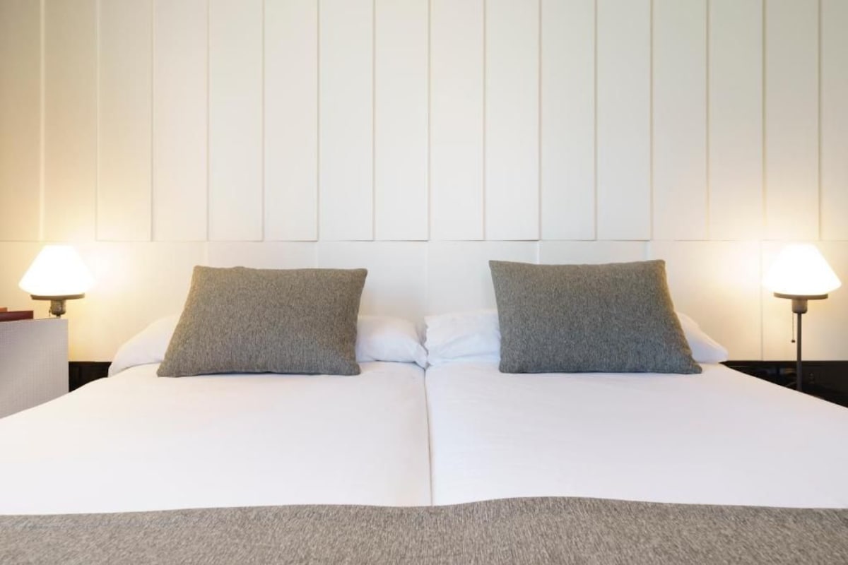 A double bed with two pillows and two bedside lamps.