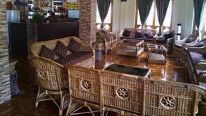 Ein großzügiger Lounge-Bereich mit Korbmöbeln, eine Bar im Hintergrund und große Fenster mit Vorhängen.
