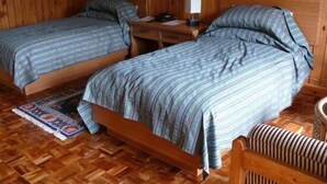 Ein Zimmer mit Holzvertäfelung, zwei Einzelbetten, einem Nachttisch mit Lampe und einem gewebten Teppich.