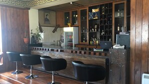 Un espace bar doté d’un plancher en bois, de tabourets de bar noirs, d’un comptoir avec un plateau en verre et d’une étagère où sont disposées diverses bouteilles et un ordinateur portable.
