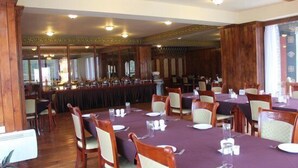 Une salle à manger avec plusieurs tables dressées, des lambris en bois sur les murs et un grand miroir qui reflète la pièce.