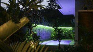 Un espacio exterior moderno con una fuente de agua, rodeado de abundante vegetación.