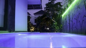 Una piscina interior con superficie de agua cristalina, rodeada por un edificio moderno con grandes ventanales y un jardín con árboles y plantas.