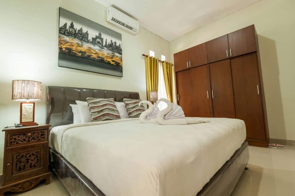A neatly made bed with white linens, a wooden headboard, and a cityscape painting above it.