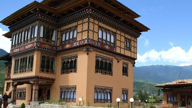 Un edificio tradicional de varios pisos con base de piedra y estructura superior de madera, que presenta diseños de ventanas ornamentales y un balcón.