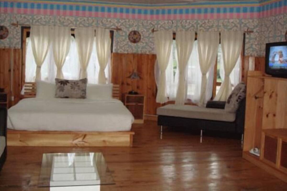 A room with a bed, a sofa, a television, and a wooden floor.