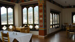 Un comedor con mesas y sillas de madera, ventanas amplias con vistas a las montañas y detalles arquitectónicos coloridos.
