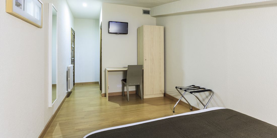 Una habitación con una cama, un escritorio, una silla, un televisor y un armario.