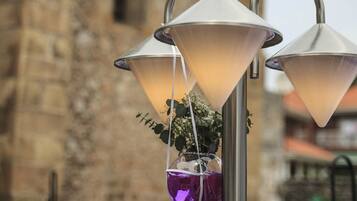 A metal lamp post with three conical lamps, a hanging purple bag, and a vase with white flowers.