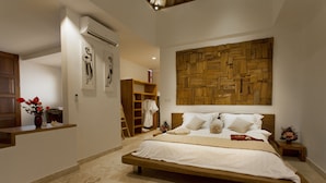 A spacious bedroom with a large bed, a wooden headboard, a wall-mounted wooden panel, a small bedside table, and a nightstand. - Villa CinCin (Canggu)