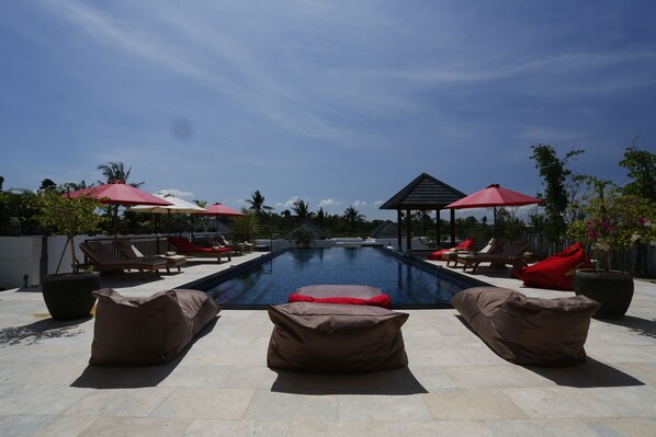A pool area with lounge chairs and umbrellas, surrounded by potted plants and a clear sky.