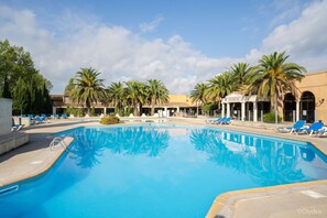 A swimming pool with lounge chairs and palm trees, surrounded by buildings with a classical architectural style. - Adonis Arles by Olydea (Arles)