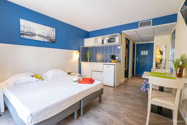 A hotel room with a bed, a desk, a kitchenette, and a bathroom. - Adonis Arles by Olydea (Arles)