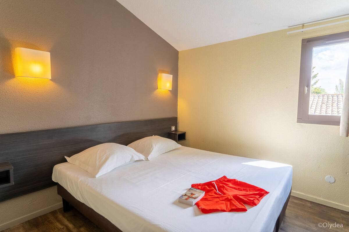 A hotel room with a bed, two wall-mounted lights, a window, and a wooden floor.
