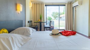 Een hotelkamer met een bed, een tafel met stoelen, een raam met gordijnen en een airconditioning.
