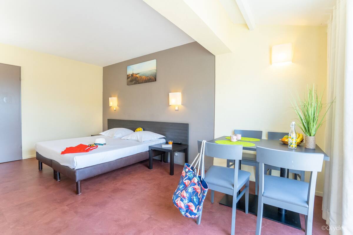 A hotel room with a bed, bedside tables, a desk with chairs, and a potted plant.