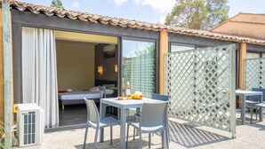 Een terras met een tafel en stoelen, een klein tafeltje met fruit, en een schuifdeur die leidt naar een slaapkamer.