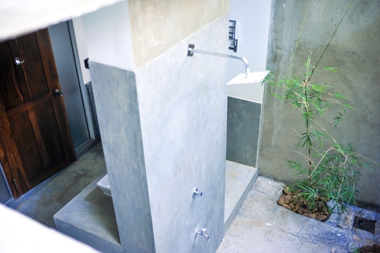 A bathroom with a toilet, a sink, and a shower area. There is a small plant on the floor.