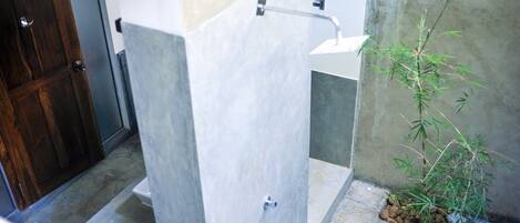 A bathroom with a toilet, a sink, and a shower area. There is a small plant on the floor.