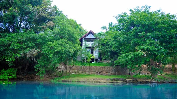 A house surrounded by lush greenery and a calm body of water. - Eliyanth Udawalawe (Udawalawa)