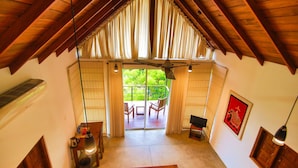 A room with a sloped ceiling, a sliding glass door leading to an outdoor patio, a small table with a lamp, and a red patterned rug. - Eliyanth Udawalawe (Udawalawa)